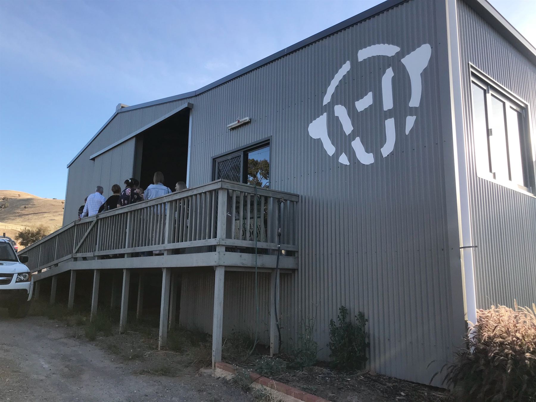 The Ashley Hills Estate cellar door building with the sheep-face logo cut into its steel wall and guests on the deck