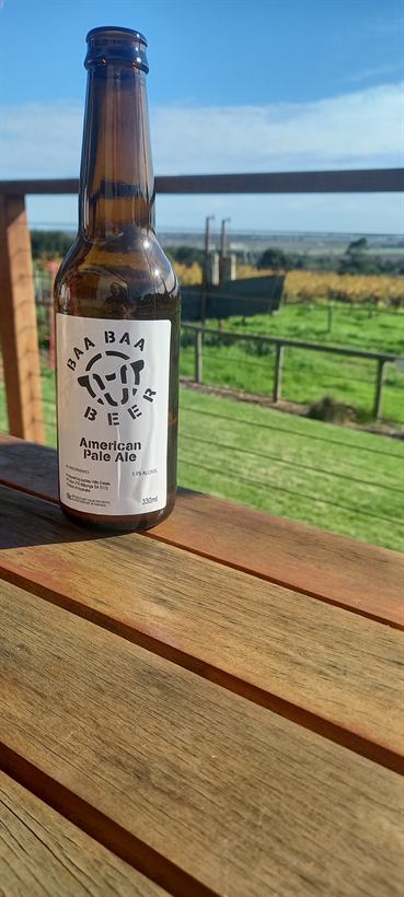 Bottle of Baa Baa beer on the deck rail above the vines