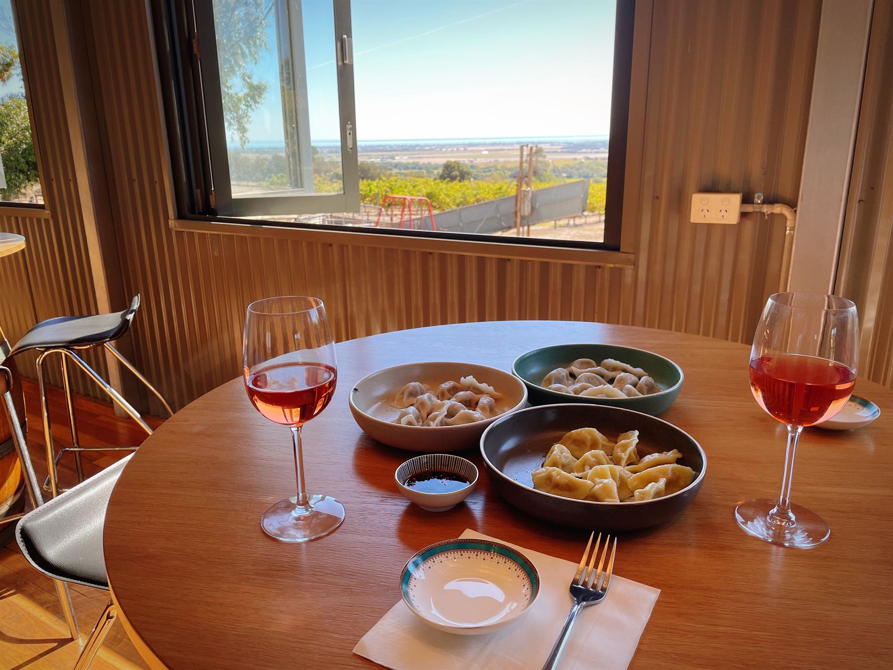 Two glasses of rosé and plates of handmade dumplings on a round table beside a window over the vines